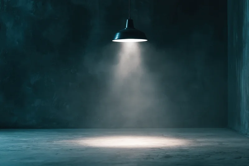 Single pendant spotlight casting a beam of light in an empty dark concrete room
