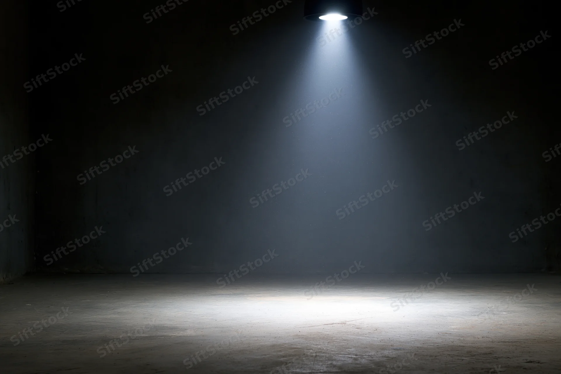 Single overhead spotlight casting a beam of light on a dark concrete floor in an empty room