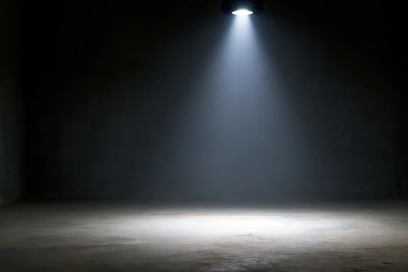 Single overhead spotlight casting a beam of light on a dark concrete floor in an empty room
