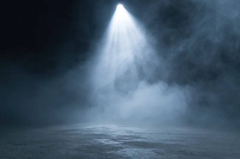 Single spotlight beam illuminating empty dark stage floor through smoke