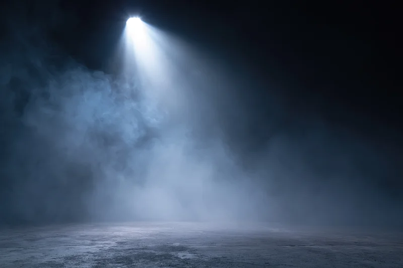 Single spotlight shining down on an empty dark stage floor through smoke
