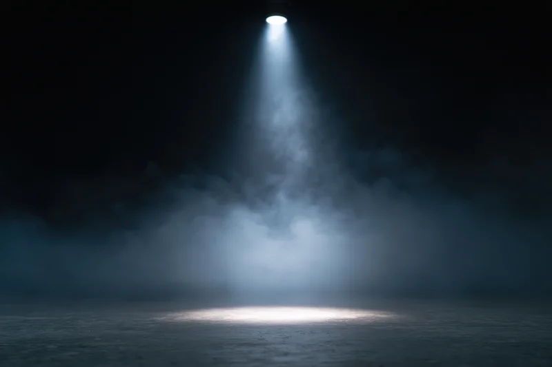 Single overhead spotlight casting a beam of light through smoke on an empty dark stage