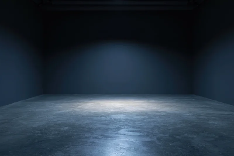 Dark empty studio room with spotlight on concrete floor and plain walls