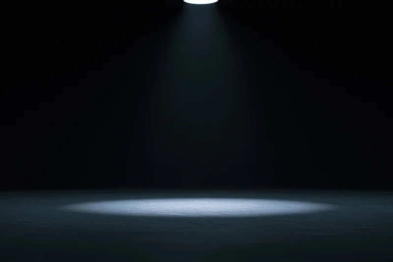 Single overhead spotlight illuminating a dark studio floor with a focused beam of light