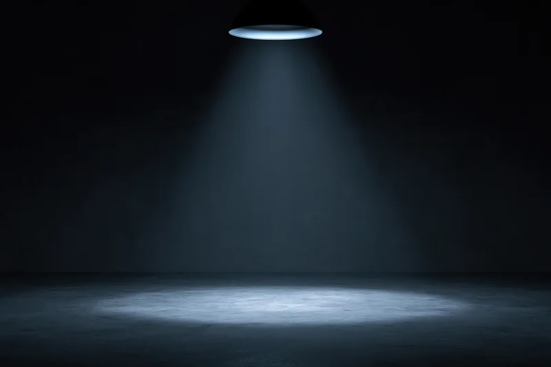Single overhead spotlight casting a blue beam on an empty dark studio floor