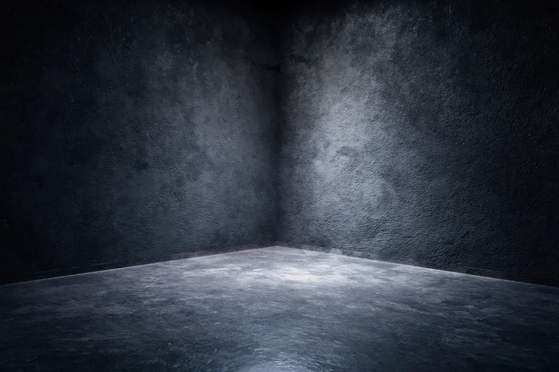Dark textured concrete corner in empty studio space with dim lighting and shadowed walls