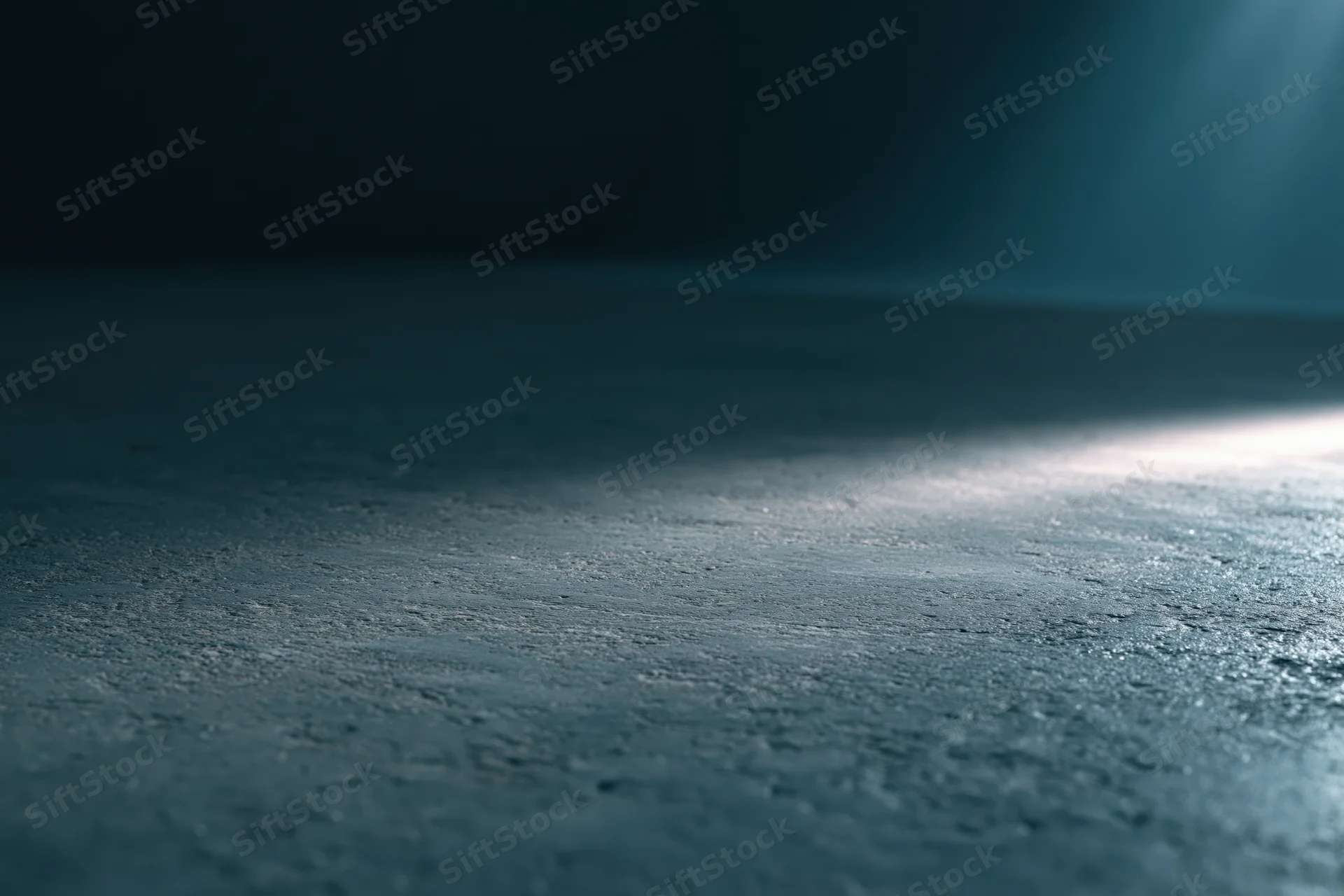 Dark studio floor with a single low horizontal beam of light creating shadow and texture