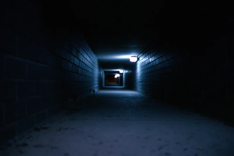 Dark urban alleyway receding into the distance at night with blue lighting and brick walls