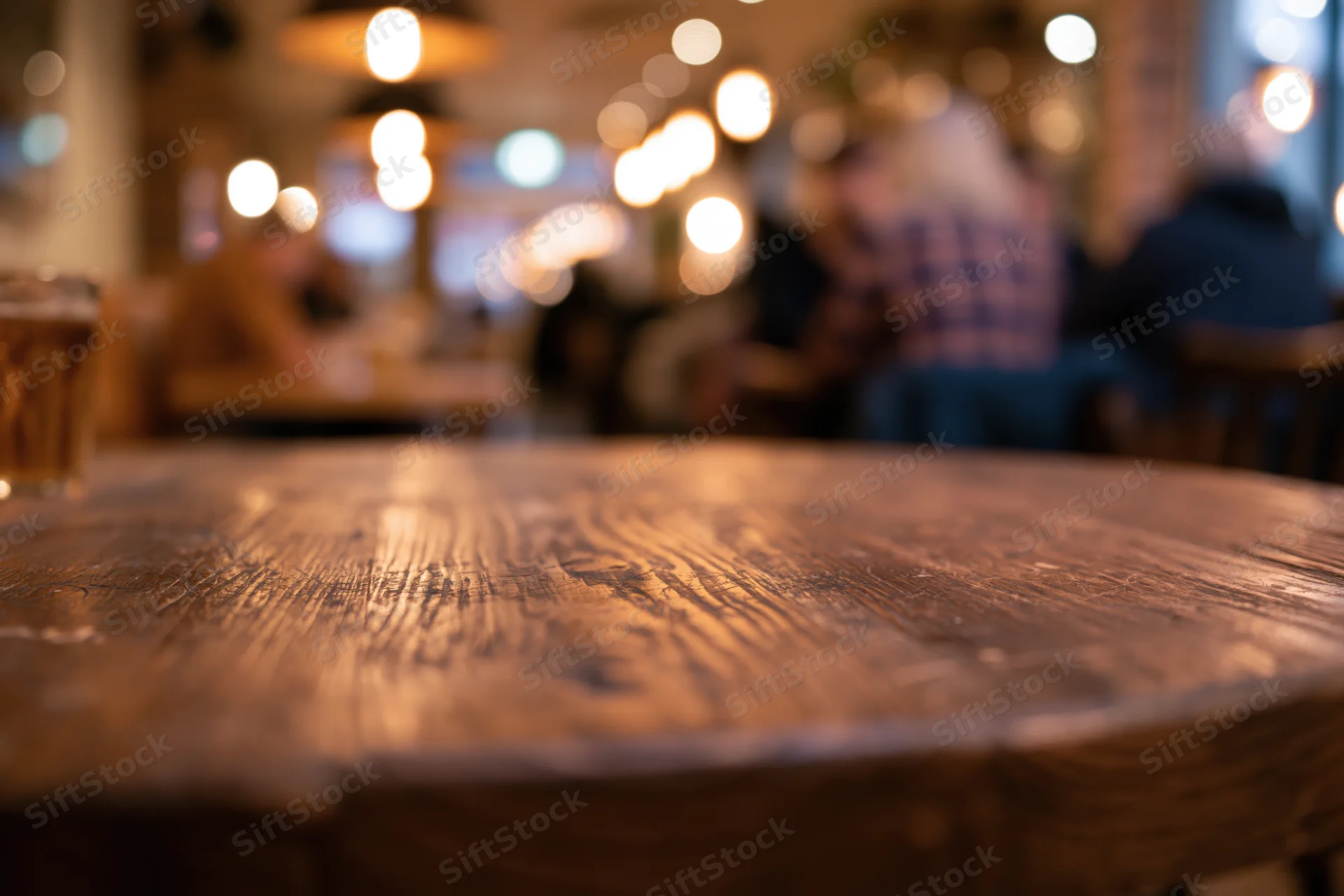 Close-up of a dark wooden table surface in a dimly lit restaurant with blurred patrons and warm lights in the background