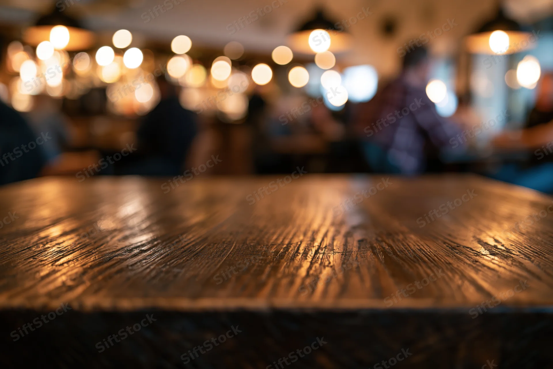 Dark wooden table surface in sharp focus with blurred restaurant interior and warm lights in background
