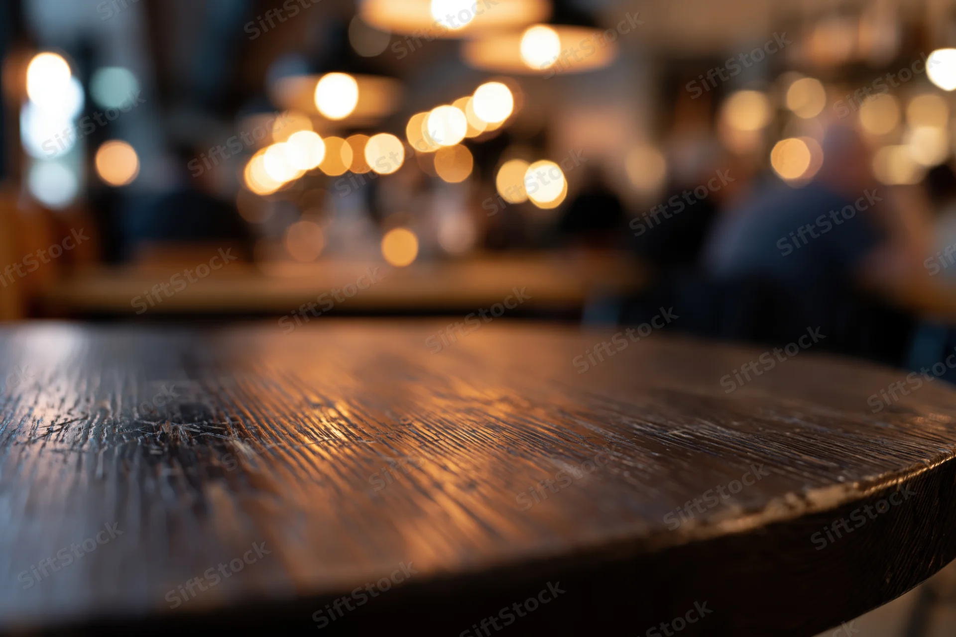 Dark wooden table surface in sharp focus with blurred restaurant interior and warm bokeh lights in background