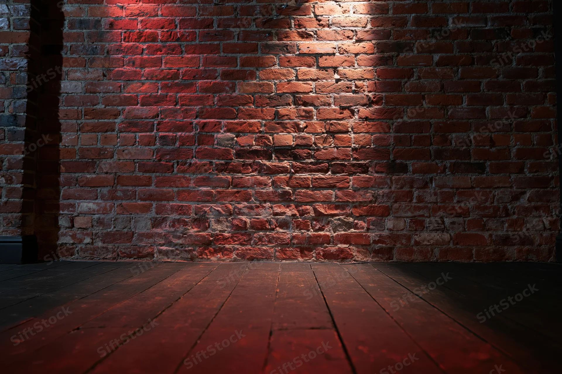 Empty room with aged red brick wall and dark wood floor under warm spotlight