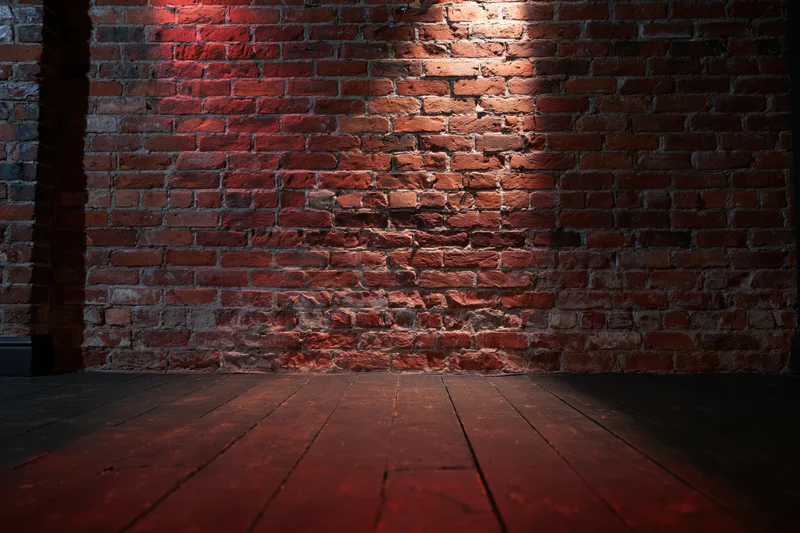 Empty room with aged red brick wall and dark wood floor under warm spotlight