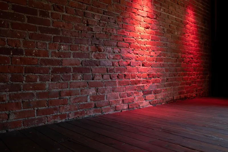 Red light illuminating an aged brick wall and dark wood floor in an empty interior room
