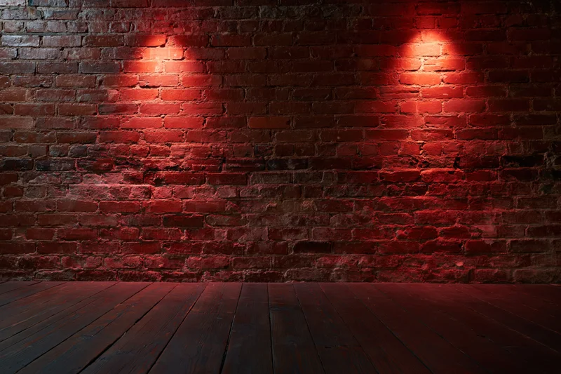 Empty room with aged red brick wall and dark wood floor under red spotlight