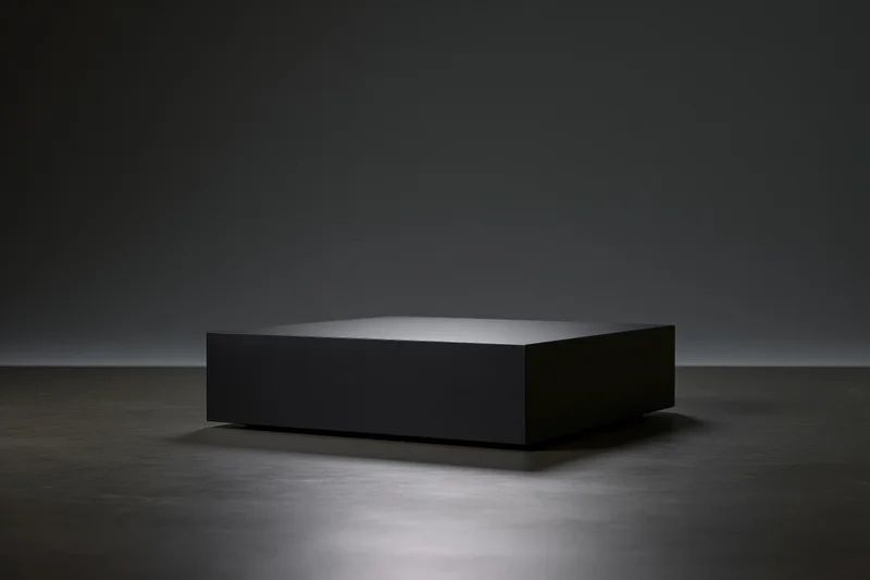 Matte black rectangular pedestal centered on a dark floor under spotlight in a studio space