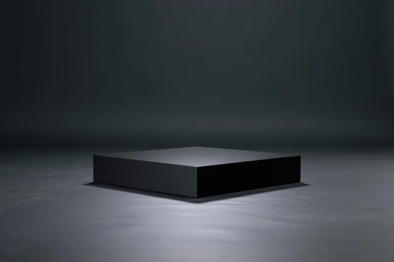 Matte black rectangular pedestal centered on a dark floor under spotlight lighting
