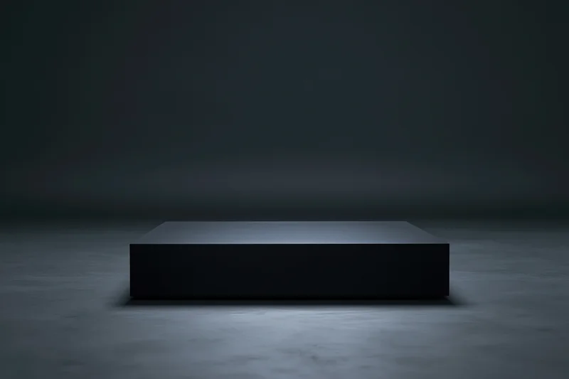 Matte black rectangular pedestal centered on a dark concrete floor under spotlight in a studio setting