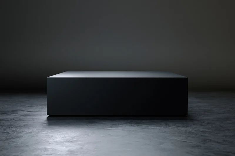 Matte black rectangular pedestal centered on a dark concrete floor under spotlight lighting