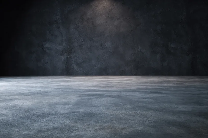 Empty industrial room with concrete floor and dark textured wall under spotlight