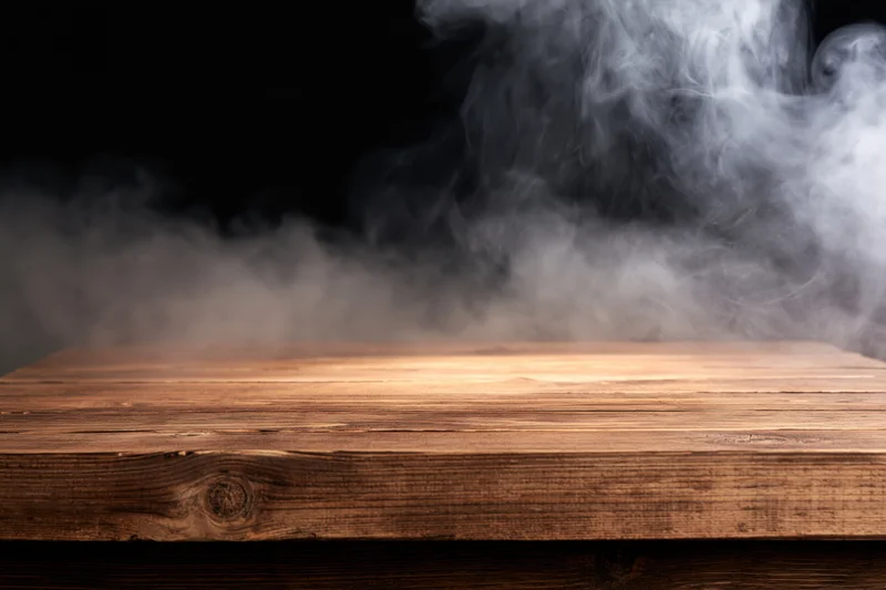 Rustic wooden tabletop with rising smoke against dark background, copyspace for product display