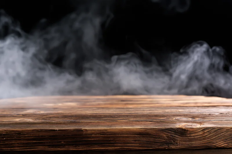 Rustic wooden tabletop with wispy smoke rising from it against a dark background