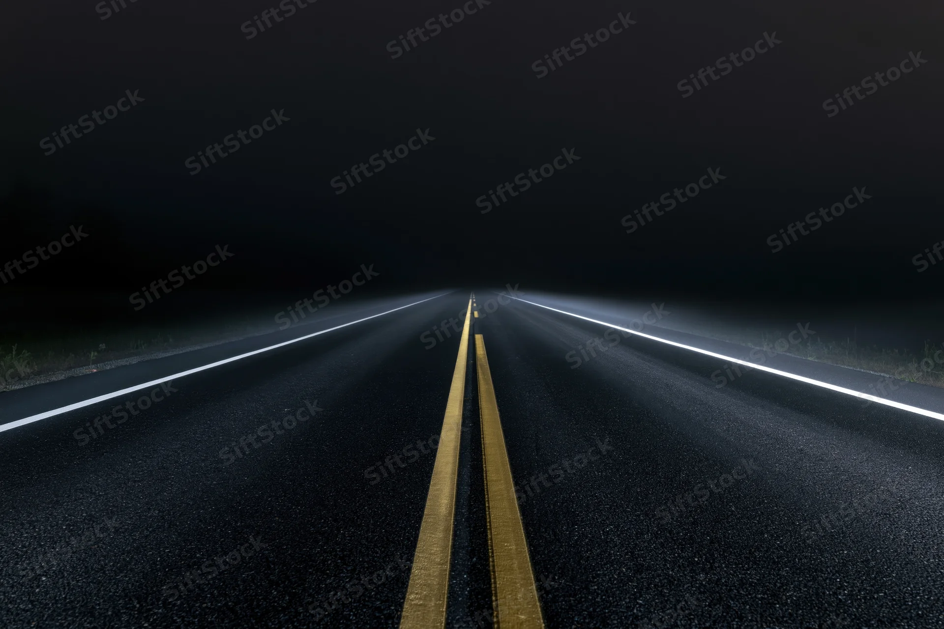 Empty asphalt road stretching into darkness at night