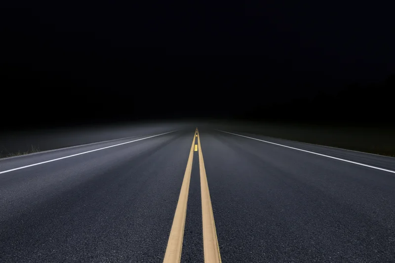 Empty asphalt road with double yellow line receding into darkness at night