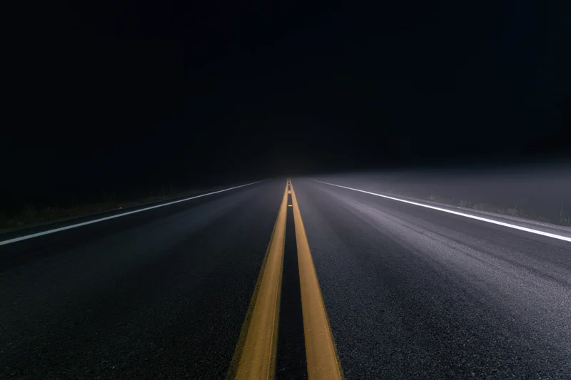 Empty asphalt road with double yellow line receding into dark fog at night