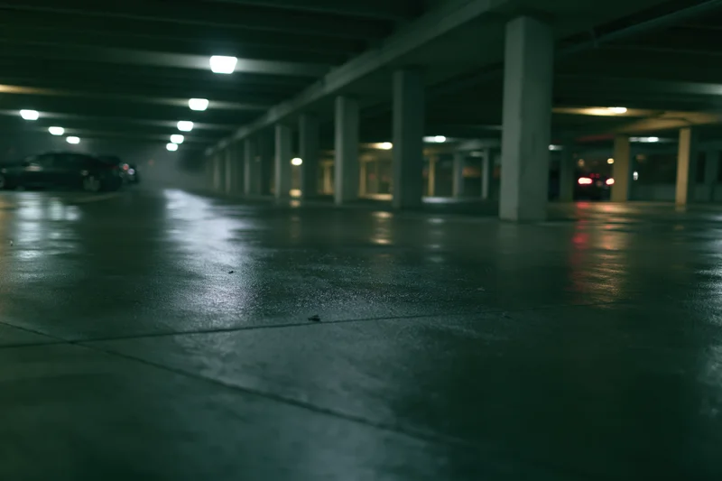 Empty underground parking garage with wet concrete floor and dim overhead lights at night