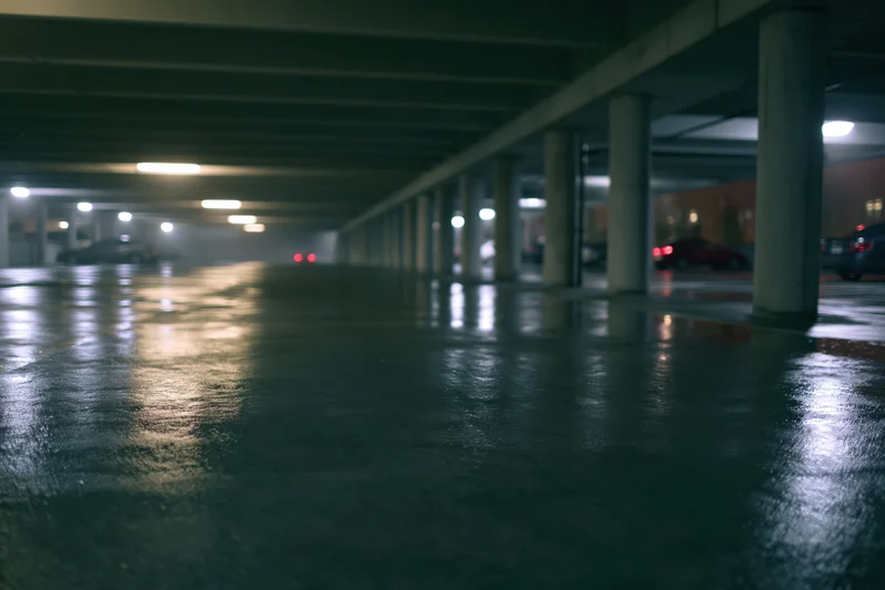 Wet concrete floor in an empty underground parking garage at night with reflections and pillars