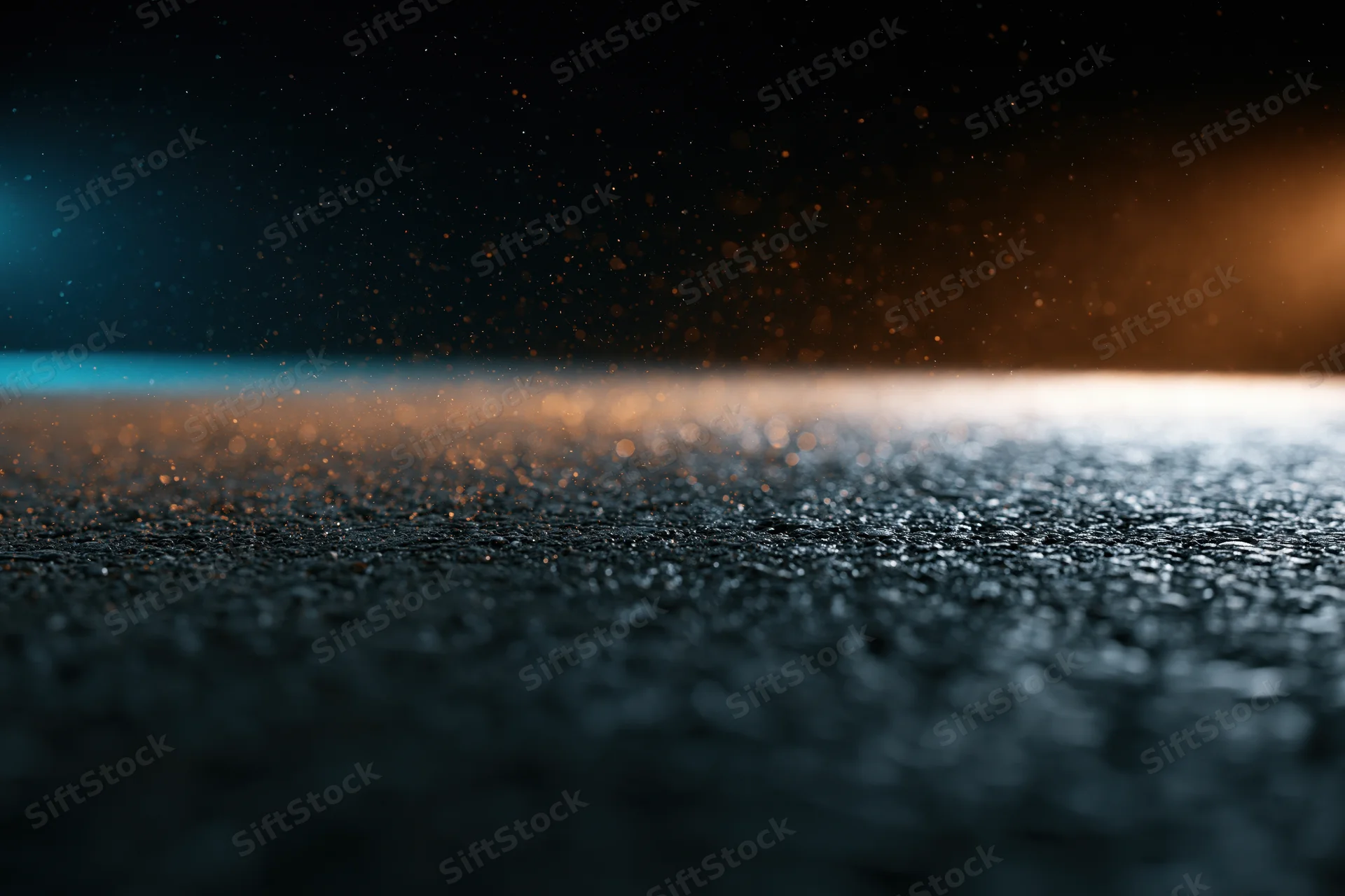 Wet asphalt surface at night with glowing light and floating particles, low angle view