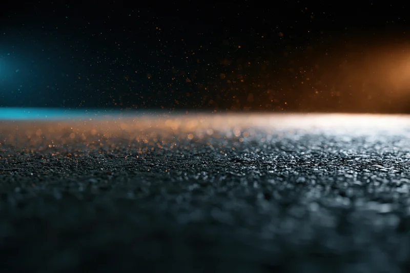 Wet asphalt surface at night with glowing light and floating particles, low angle view