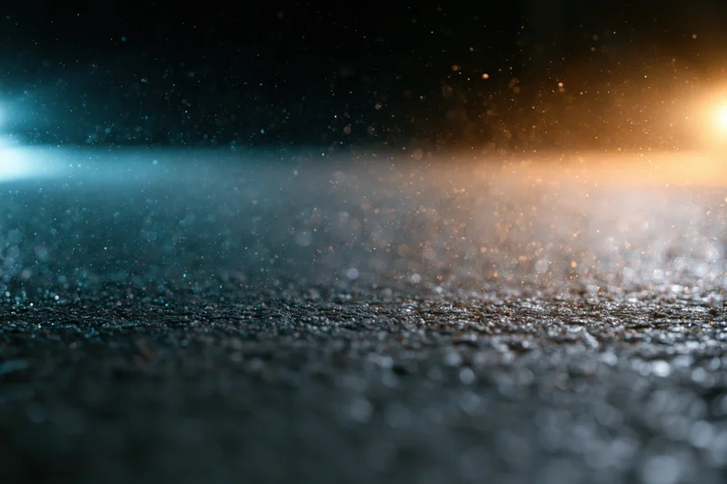 Wet asphalt surface at night with rain droplets and light reflections, low angle view