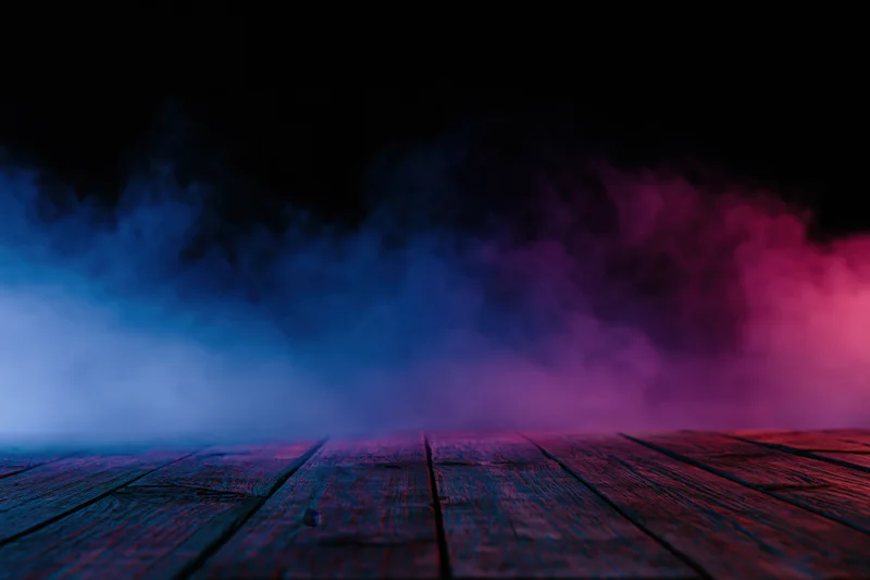 Low-angle view of wooden floor with blue and pink smoke against black background