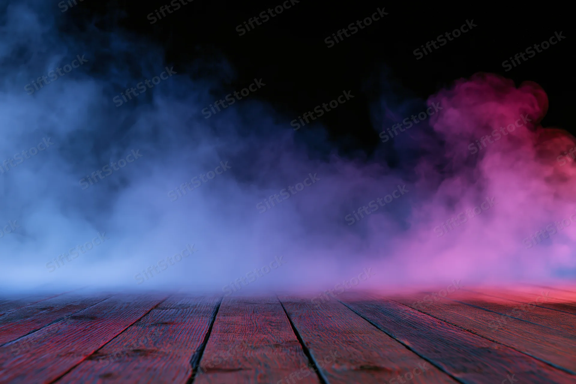 Low-angle view of wooden floor with blue and pink smoke against black background