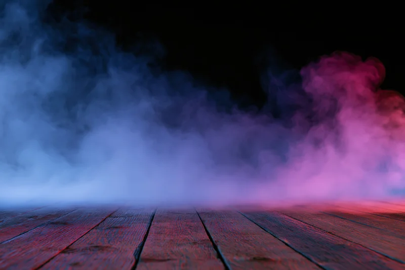 Low-angle view of wooden floor with blue and pink smoke against black background