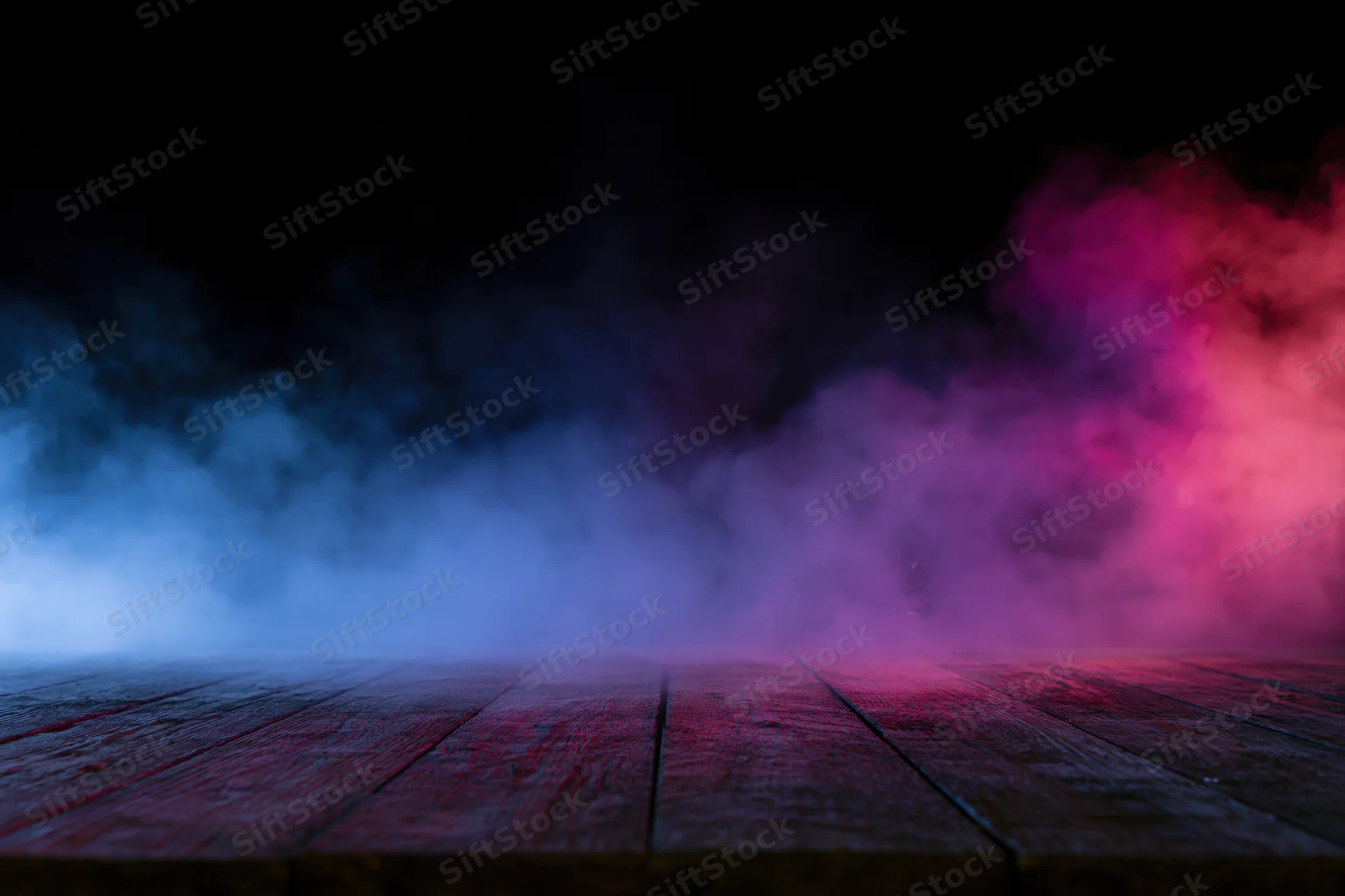 Low-angle view of empty wooden floor with blue and pink smoke against black background