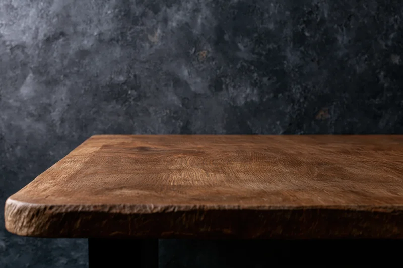 Wooden tabletop with visible grain and rounded edge against dark textured wall