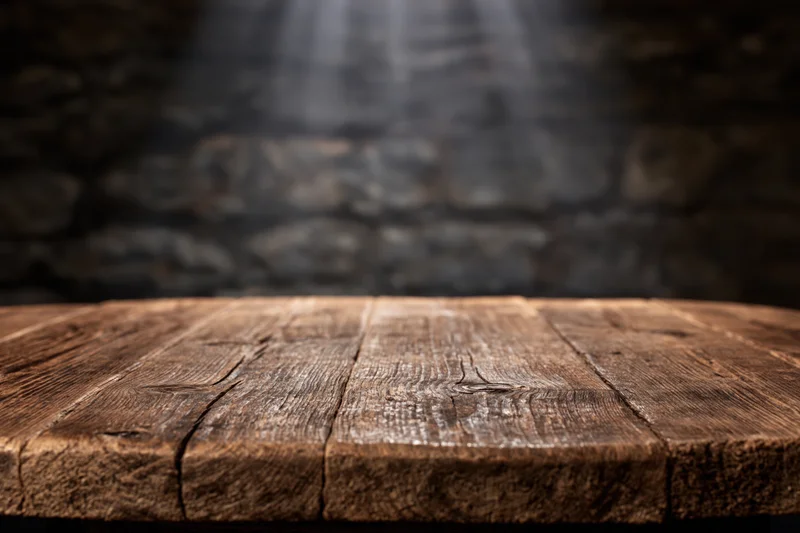 Worn wooden tabletop in front of dark stone wall with spotlight beam
