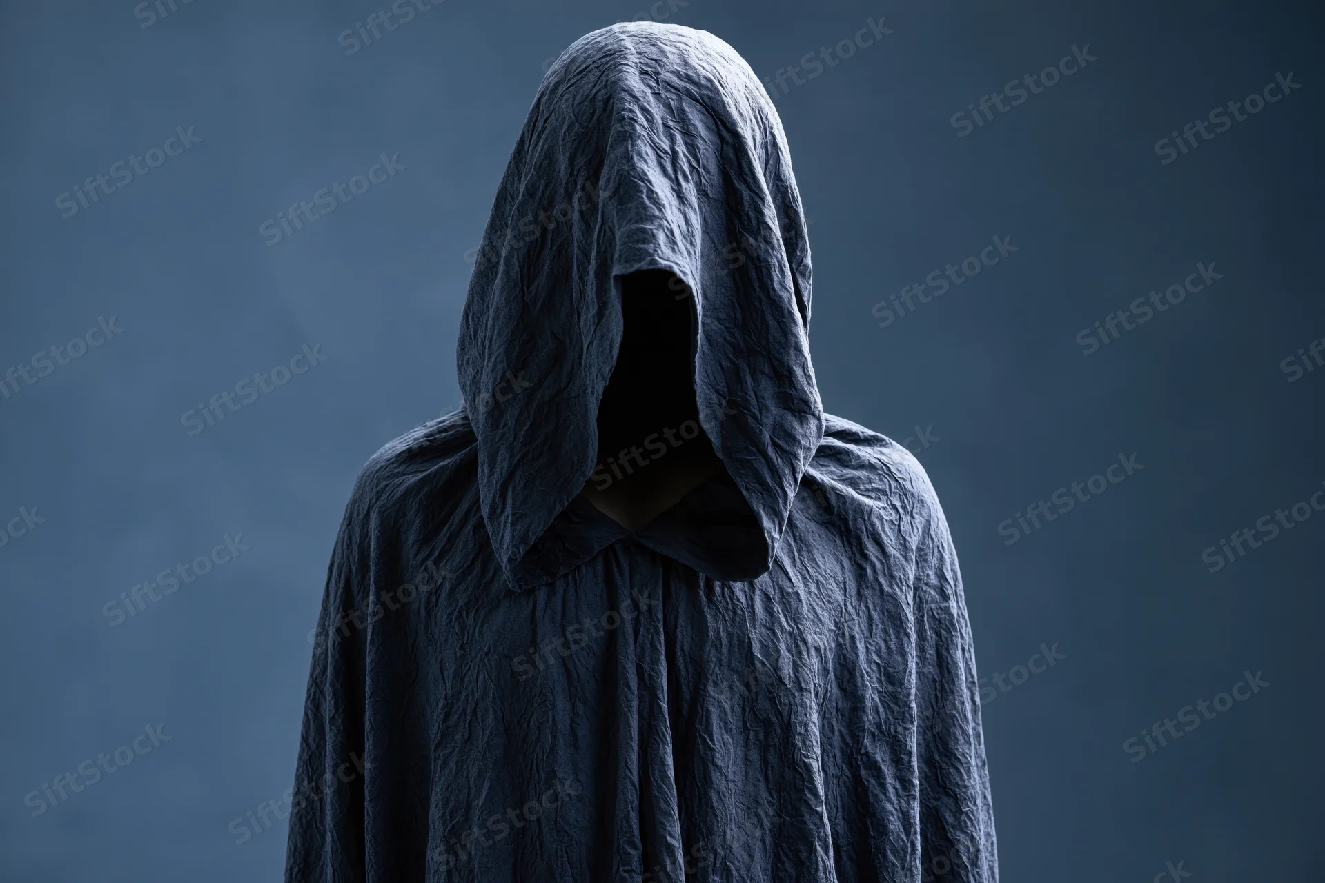 Faceless hooded figure standing still in dark smoky atmosphere