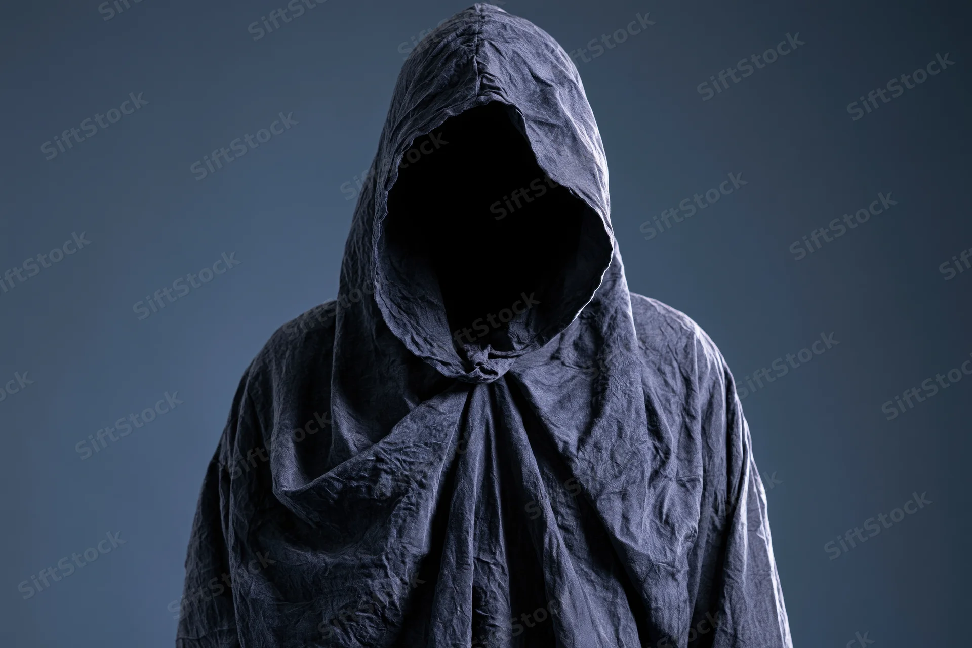 Hooded figure with face completely hidden standing in studio setting