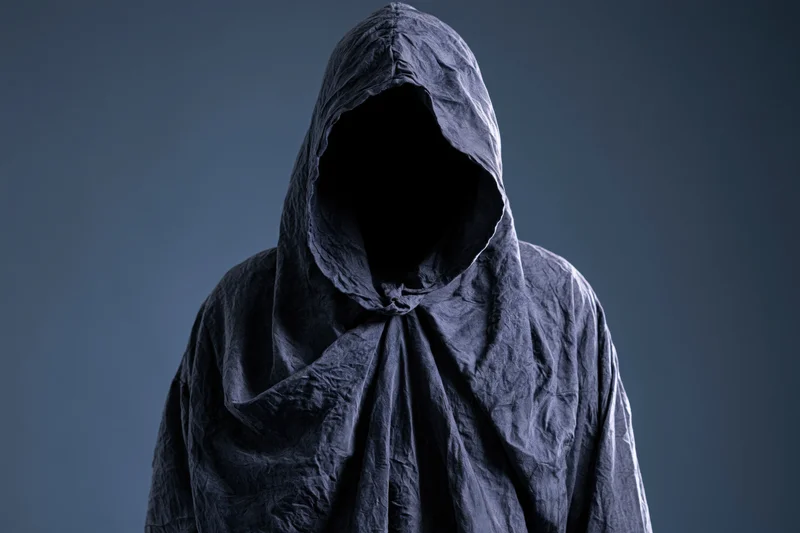 Hooded figure with face completely hidden standing in studio setting