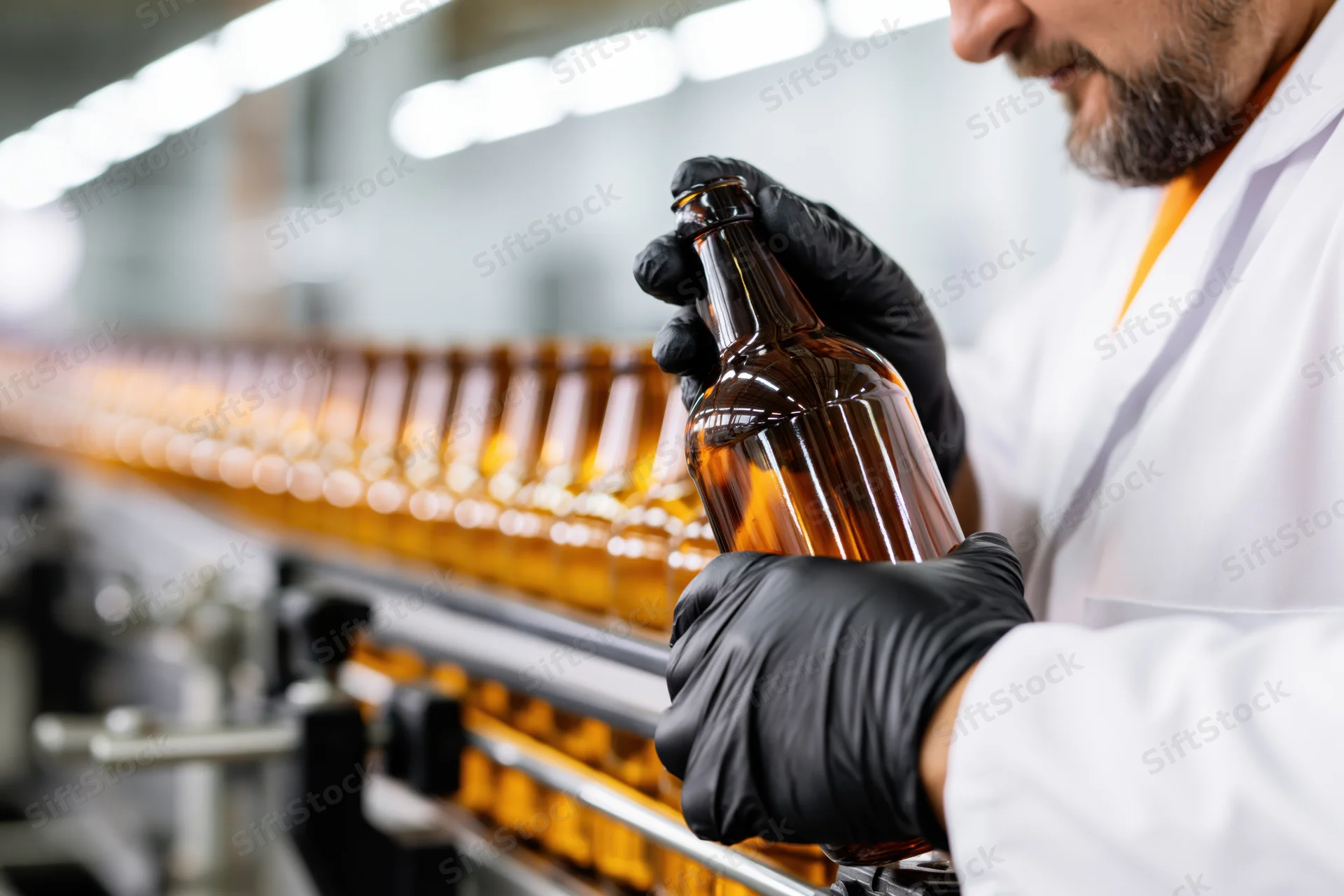 Man in lab coat inspecting brown glass beer bottle on conveyor line in factory