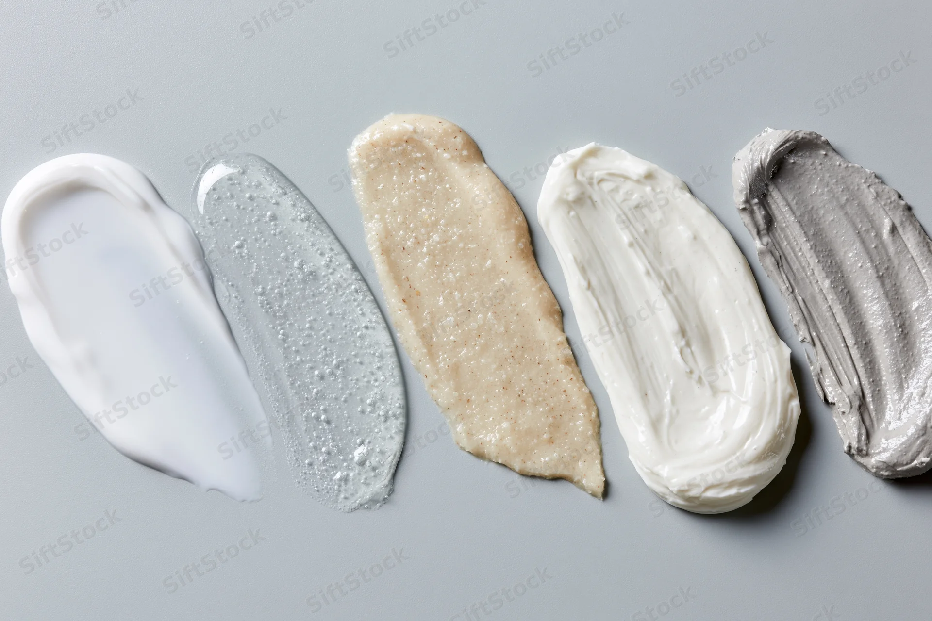 Five skincare cream smears arranged in a row on a flat surface