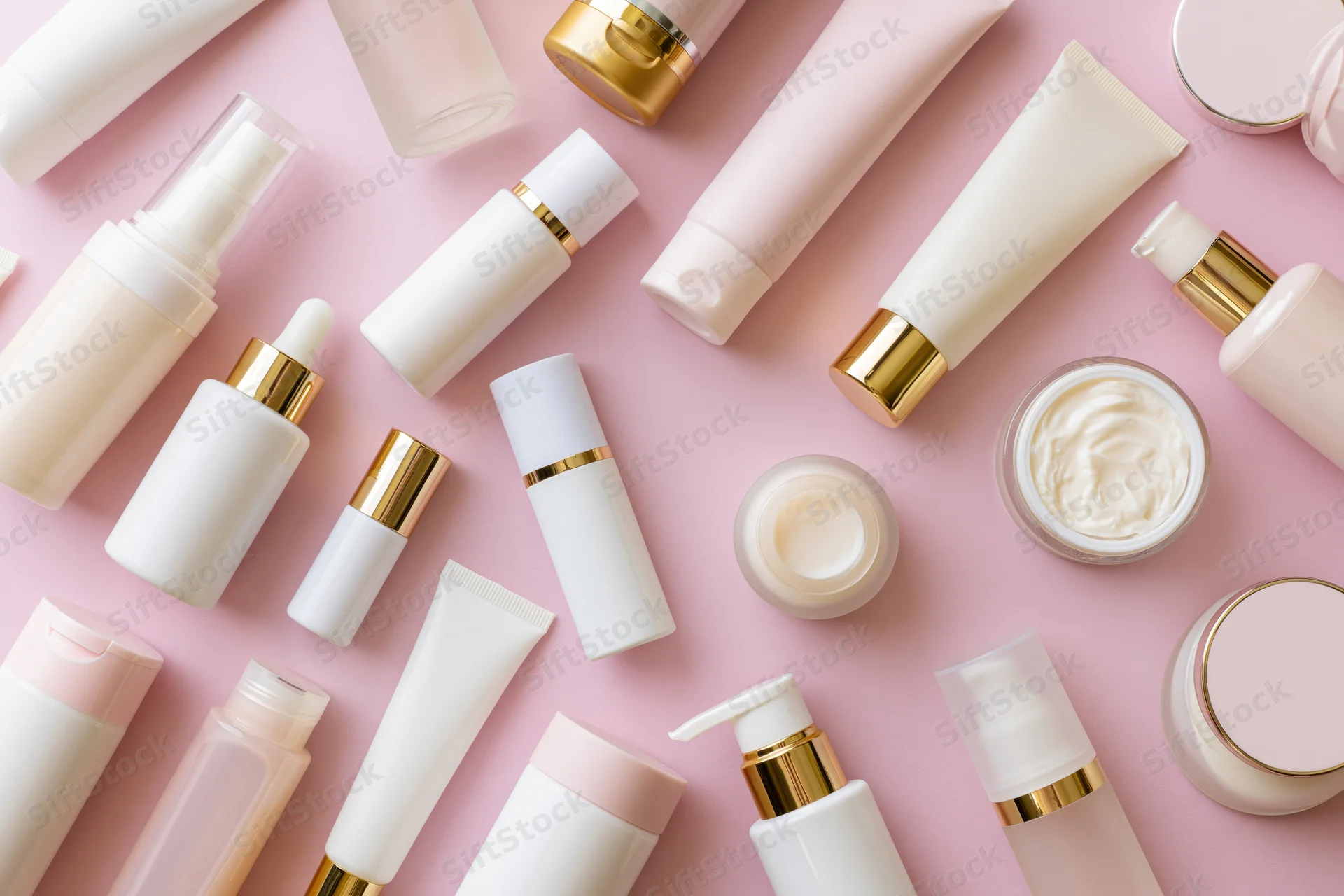 Flat lay of skincare and beauty products arranged on pink background