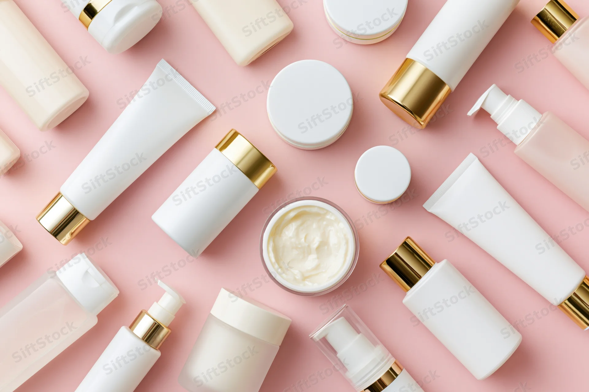 Flat lay of skincare and beauty products arranged on pink background with copyspace
