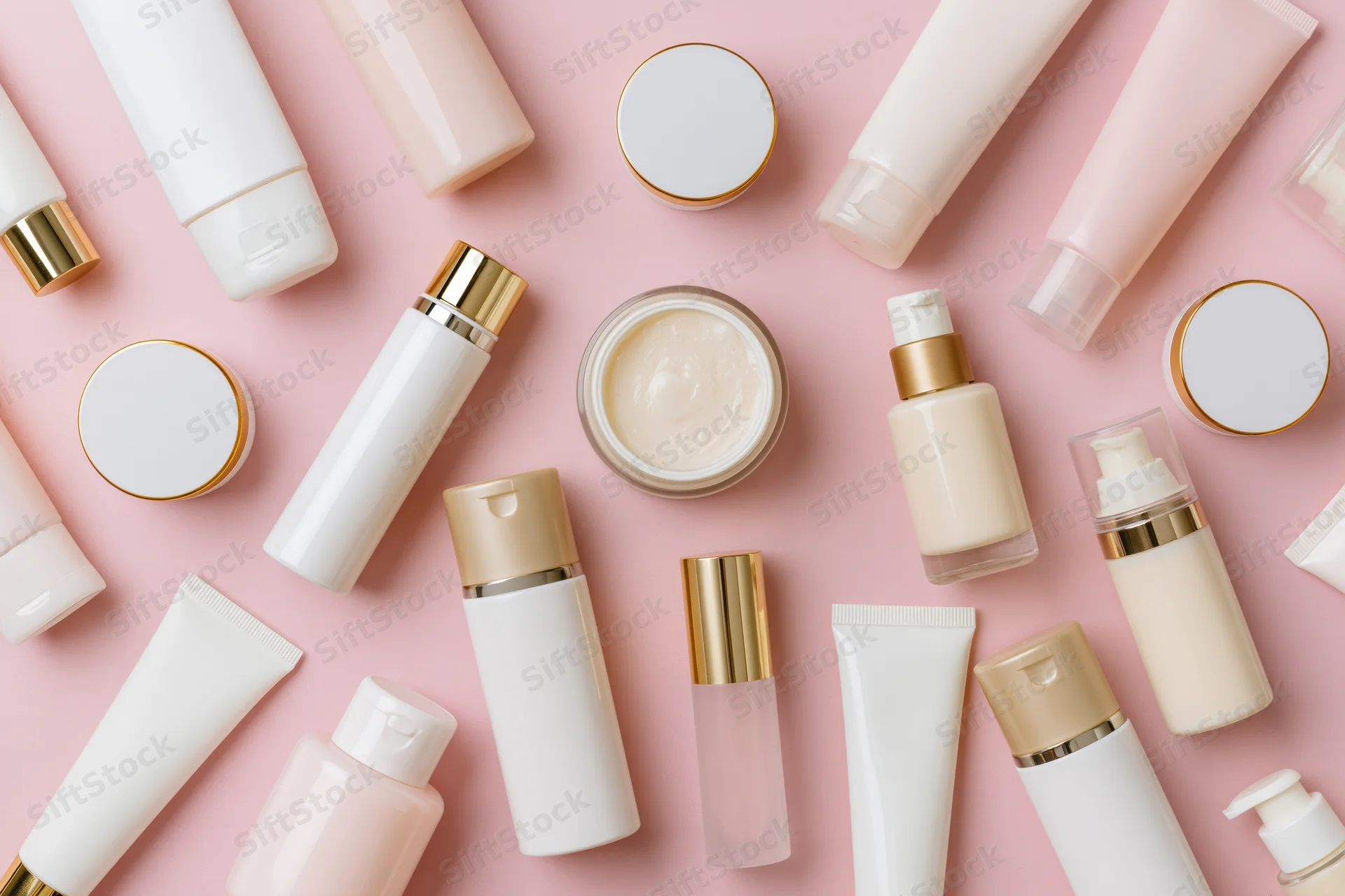Flat lay of skincare and beauty product bottles and jars on pink background