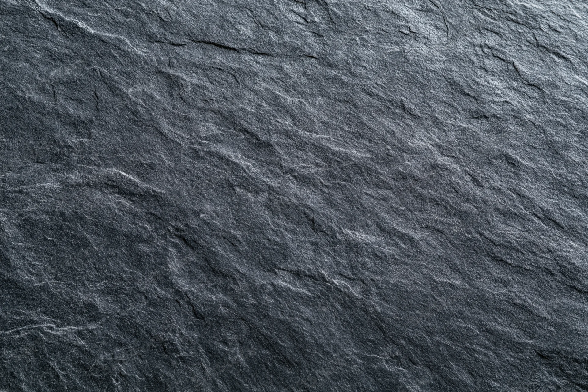 Close-up of dark slate stone surface with natural texture and grain filling the frame