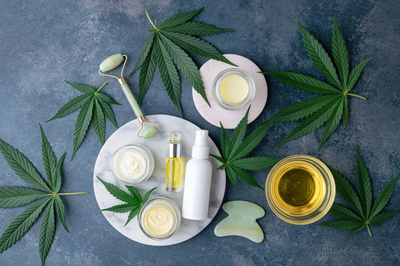 Cbd skincare products arranged on a marble tray with cannabis leaves and beauty tools